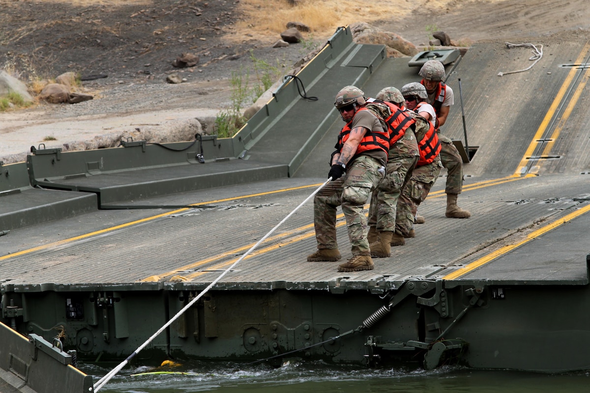 Soldiers pull on a cable while shifting a ramp to dismantle a 100-foot temporary floating bridge.