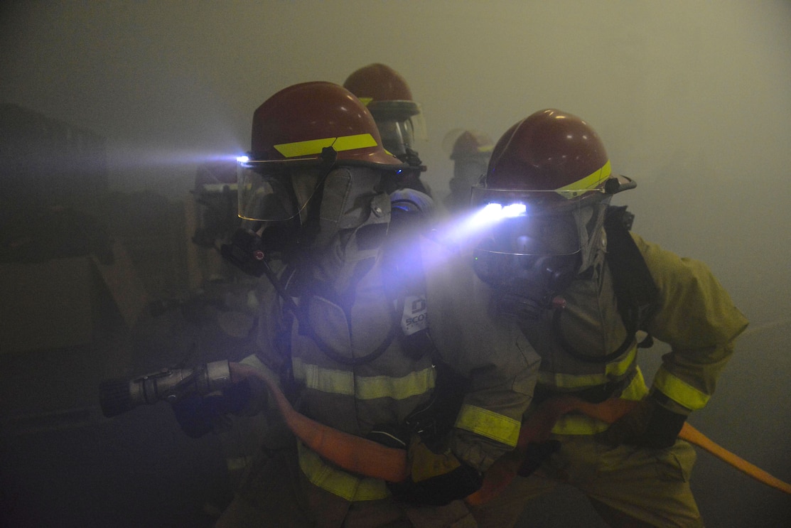 sailors in firefighter attire storms in a stimulation with smoke around them