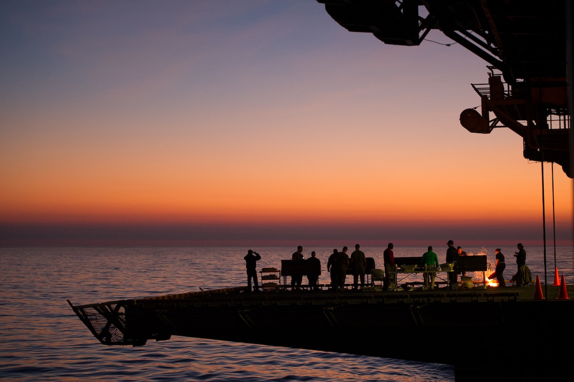 Silhouette of sailors standing on the ship, barbequing, chatting and hanging out with scenery of ocean sunset in the background