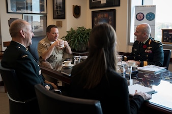 U.S. Navy Vice Admiral and Canadian Armed Forces personnel sit and laugh at table in office