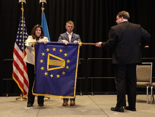 Two people unrolling a blue flag with yellow details while a third person holds the flag horizontally.