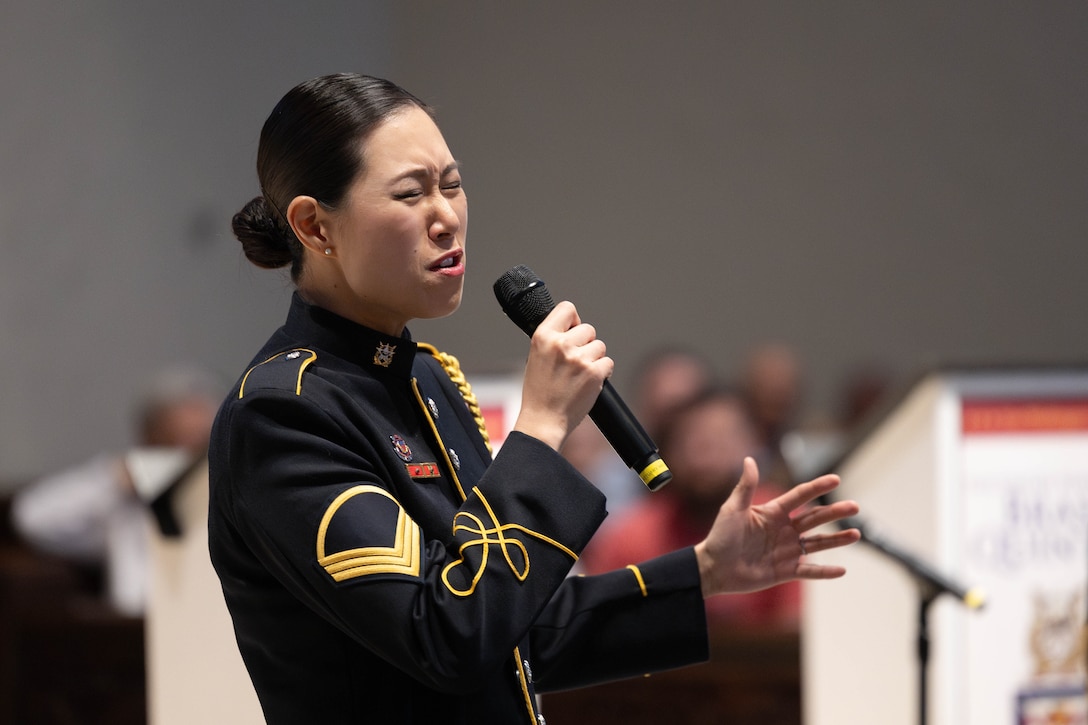 A soldier in a formal uniform holds a microphone and sings.