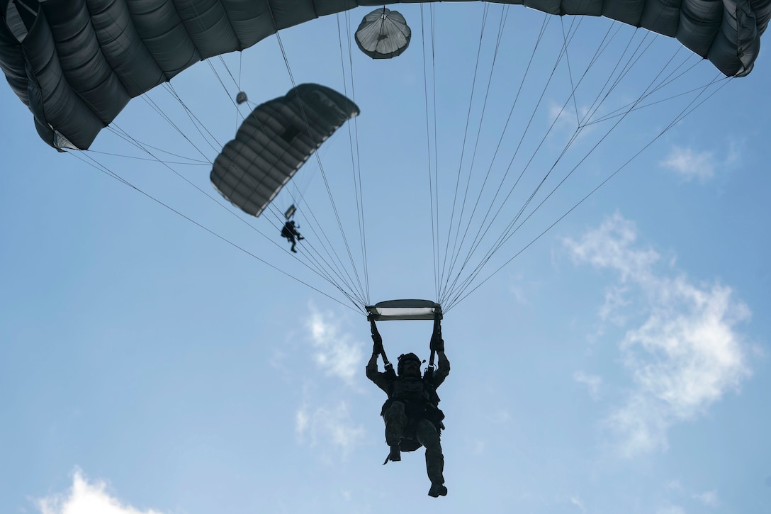 Two airmen parachute to the ground against a light blue sky.