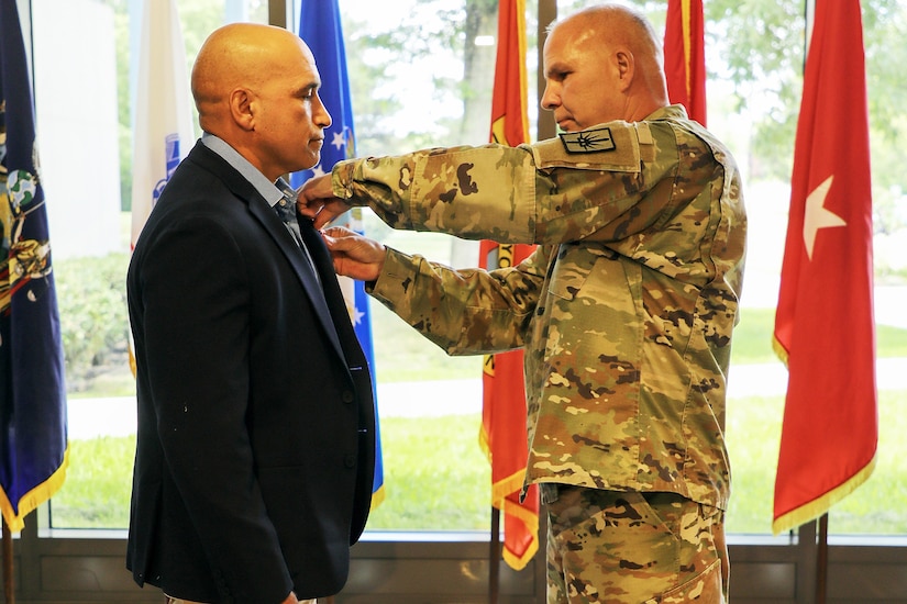 A service member pins a medal on a veteran dressed in business attire.