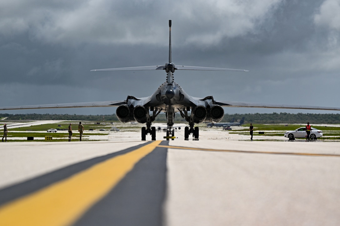 An aircraft sits on the tarmac as personnel walk near it under a gloomy sky.