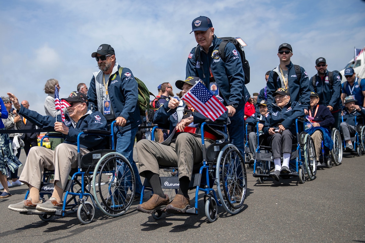 Civilians push veterans in in wheelchairs past a crowd of well-wishers on a flight line.