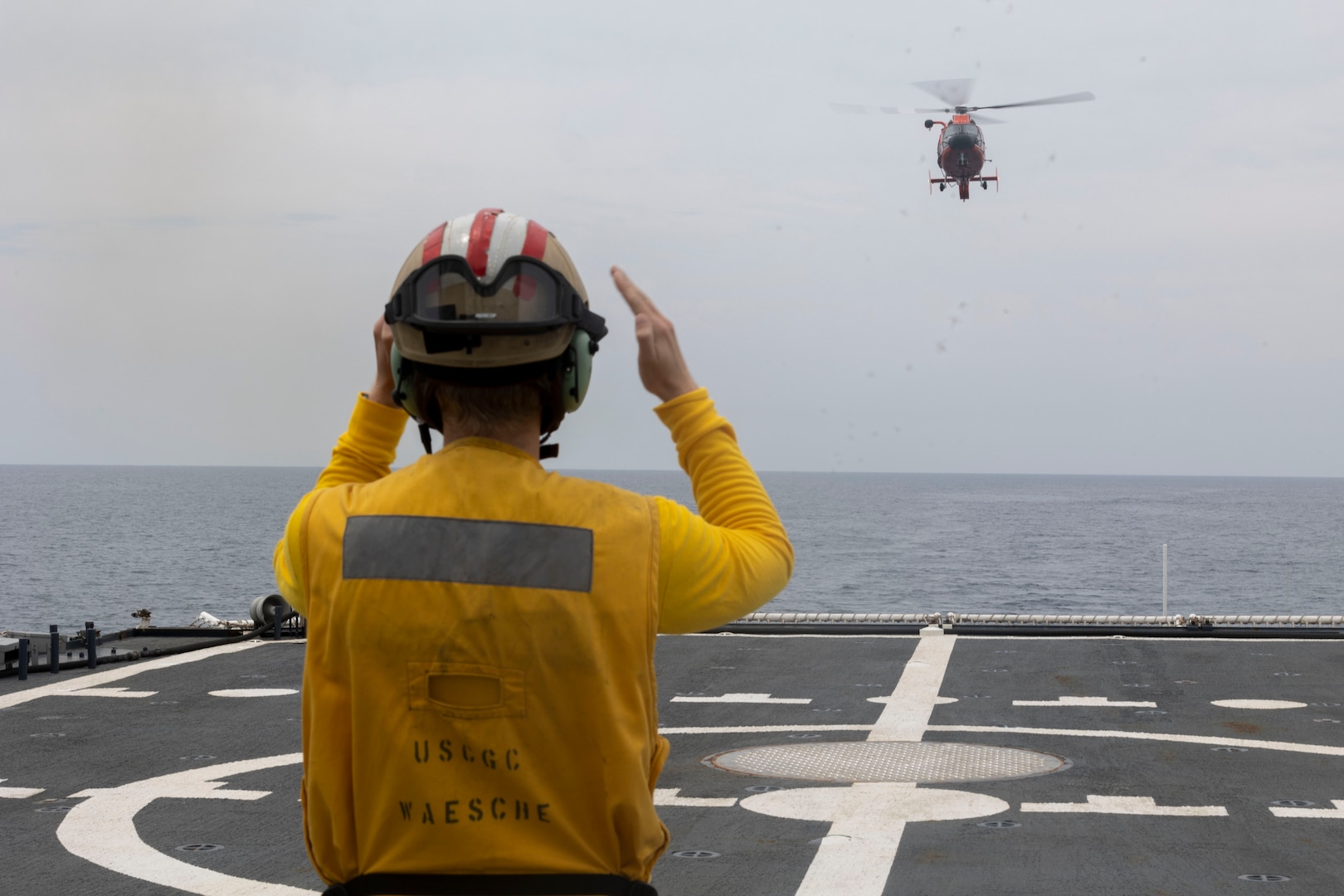 U.S. Coast Guard Ens. Henry Arnold, a deck watch officer assigned to the U.S. Coast Guard Cutter Waesche (WMSL-751), guides a U.S. Coast Guard MH-65E helicopter onto the flight deck of the Waesche during a trilateral search and rescue exercise in the East Sea, June 6, 2024. Coast Guardsmen from Japan, Republic of Korea, and the United States participated in the first joint trilateral search and rescue exercise between the three nations, working together to improve interoperability when responding to a real-world crisis. The U.S. Coast Guard has operated in the Indo-Pacific for more than 150 years, and the service is increasing efforts through targeted patrols with our National Security Cutters, Fast Response Cutters and other activities in support of Coast Guard missions to enhance our partnership. (U.S. Marine Corps photo by Cpl. Elijah Murphy)