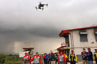 A photo of a firefighter drone in the sky with people looking up at it.