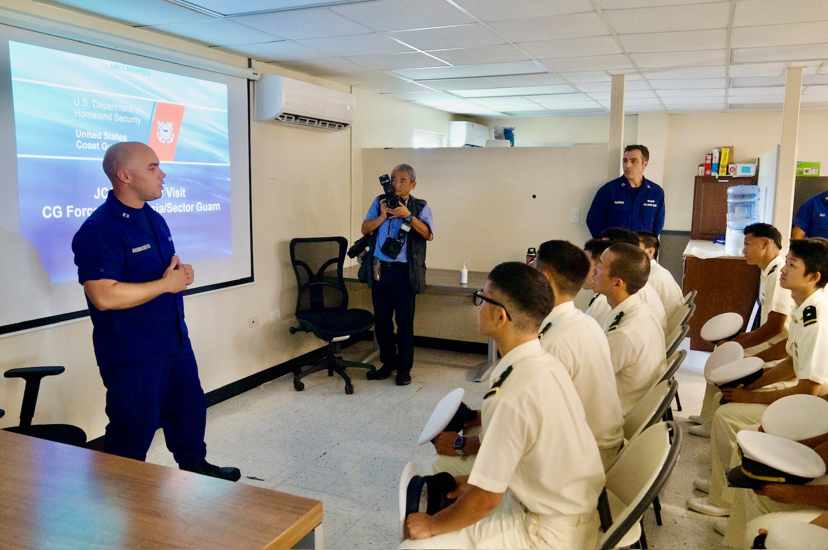 Lt. Jay DeInnocentiis gives an overview of waterways management at U.S. Coast Guard Forces Micronesia Sector Guam as they host Capt. Kazushi Sakae and over 40 cadets from the Japanese Coast Guard training ship Kojima during their visit to Guam on June 12, 2024. The event marked a significant moment of international cooperation and camaraderie between the two maritime services. (U.S. Coast Guard photo by Josiah Moss)