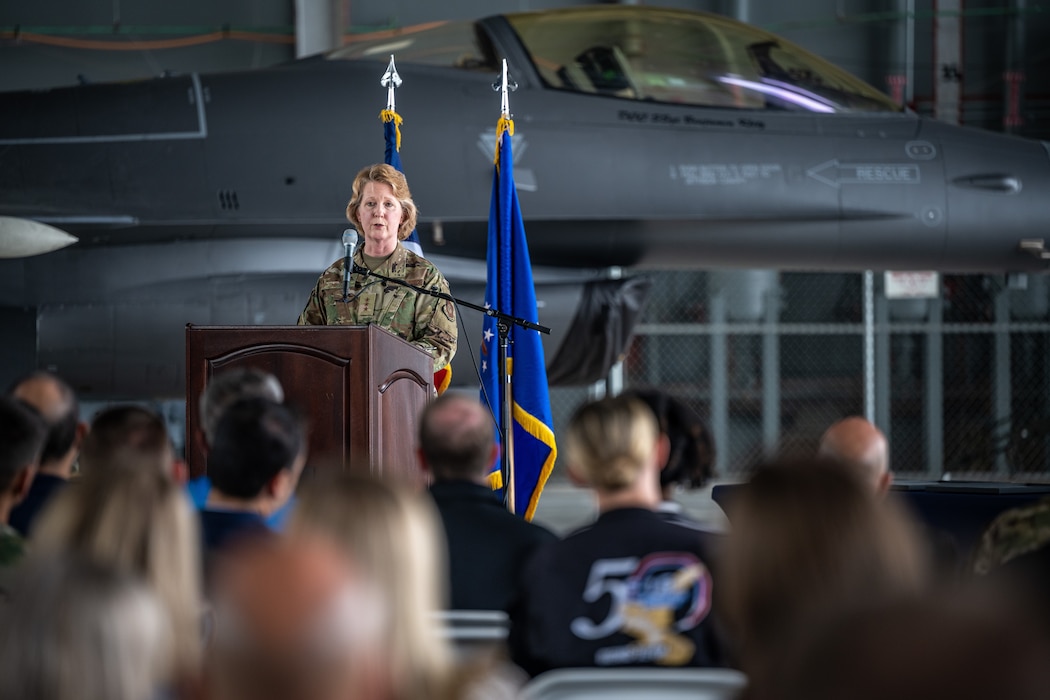 Female general stands on stage in front of plane.