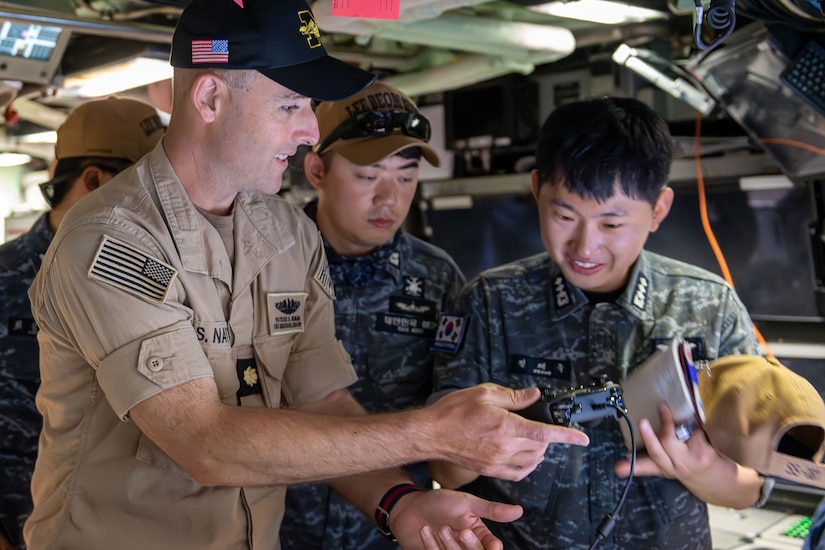 A U.S. sailor shows a device to two South Korean sailors inside a submarine.