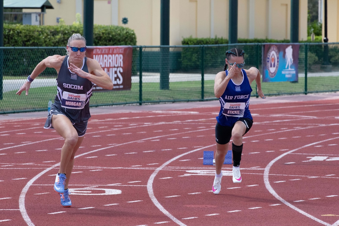 Two athletes race side by side on a track with a building in the background.