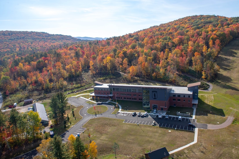 A large schoolhouse sits on a hillside among fall foliage.